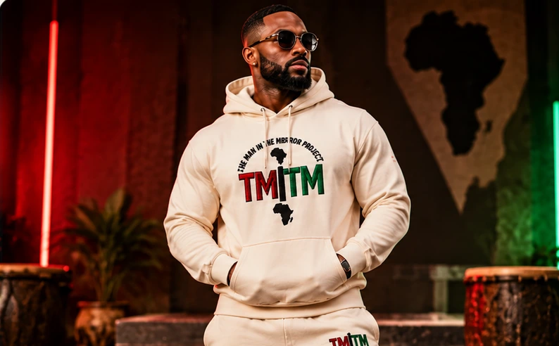 Black male model wearing a cream TMITM hoodie and matching tracksuit